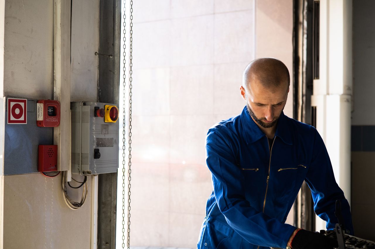 Technician in blue overalls beside an electrical control panel