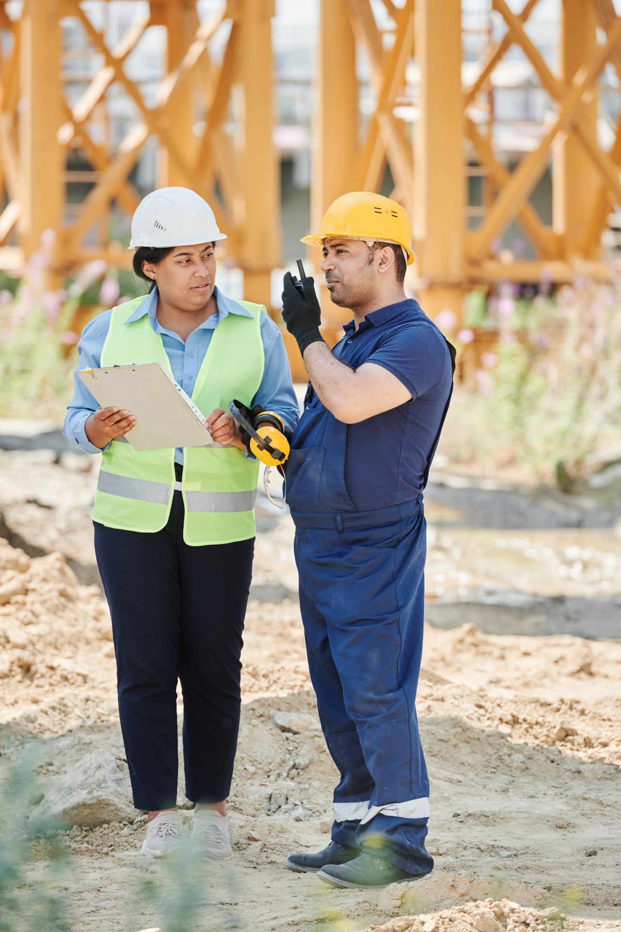 Two site professionals in hard hats reviewing a clipboard outdoors